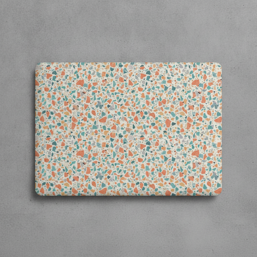 AI laptop skin design generator result: a laptop lid seen straight down, wrapped in a matte vinyl skin printed with a dense terrazzo scatter of coral, teal, mustard and grey chips on cream, the pattern running off all four rounded corners with no border