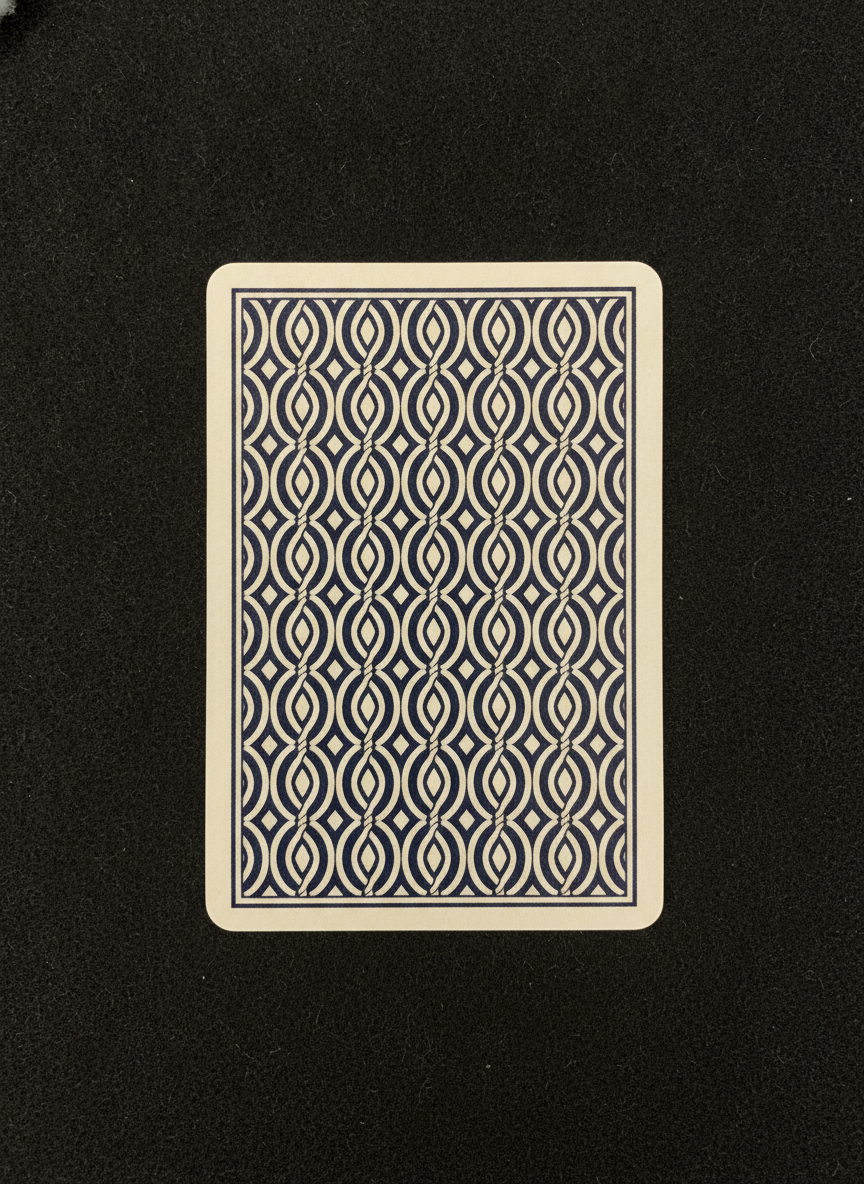 AI playing card design generator result: a navy and cream card back on black felt, columns of interlocking ribbons with small diamonds between them, held inside a thin navy rule and an even cream border of equal width on all four sides